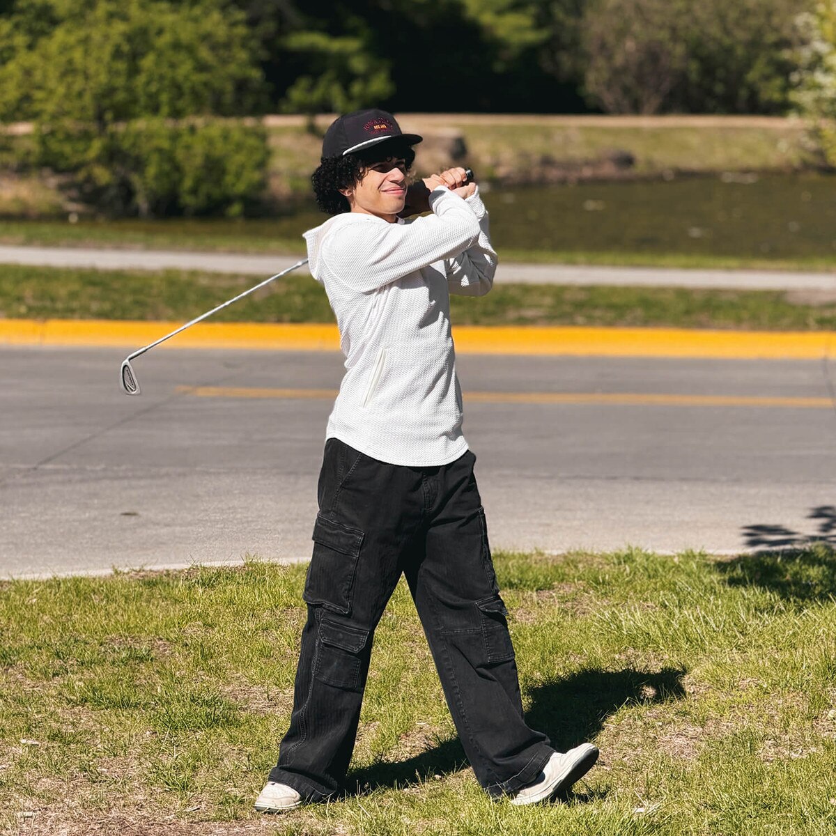 Student finishing a golf swing while wearing Swannies I-State White Camden Hooded Sweatshirt